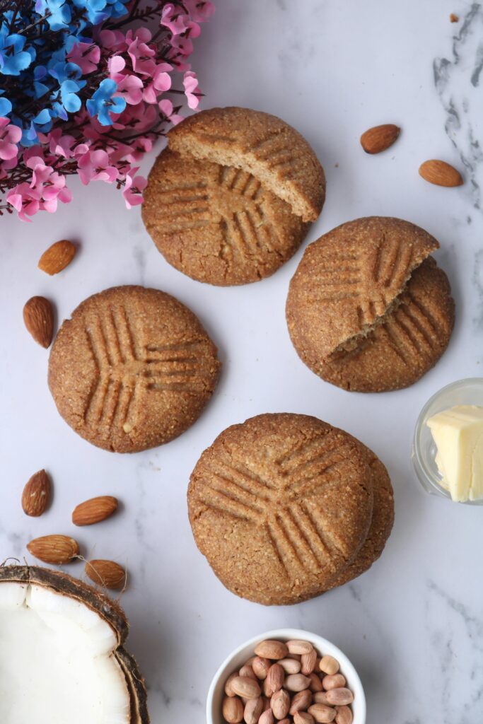 Delicious peanut butter cookies surrounded by almonds and coconut on a marble surface.
