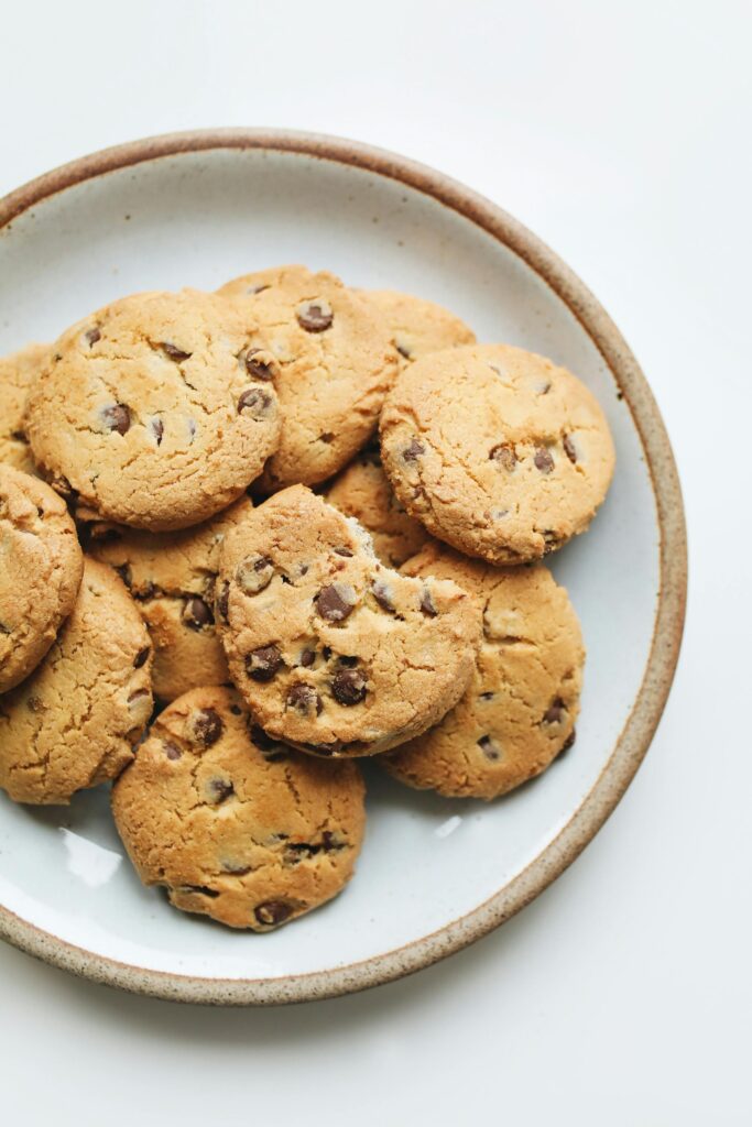 A stack of homemade chocolate chip cookies in a rustic ceramic bowl on a light background.